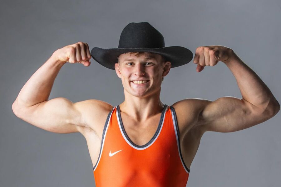 Benji Mower in an orange Oklahoma State singlet and black cowboy hat, smiling and flexing both arms