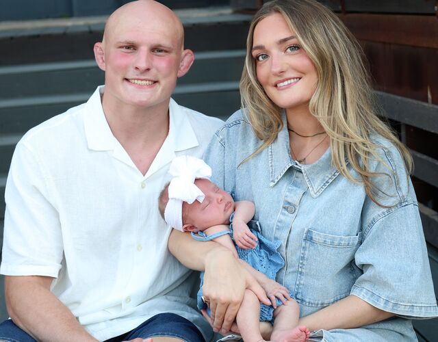 Benji smiling with his family, holding their baby